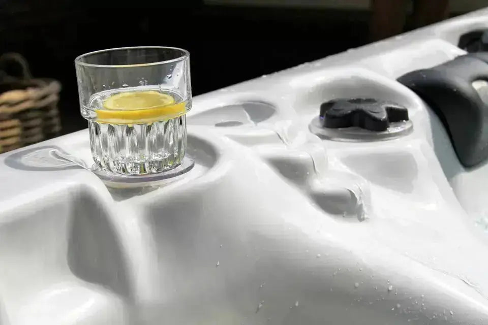 Witte jacuzzi buiten met bekerhouder en glazen waterglas gevuld met water en citroen, spa voor 5 personen.