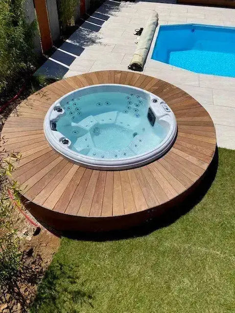 Ronde buitenjacuzzi met houten omlijsting, 7-persoons swimspa naast zwembad in tuin.