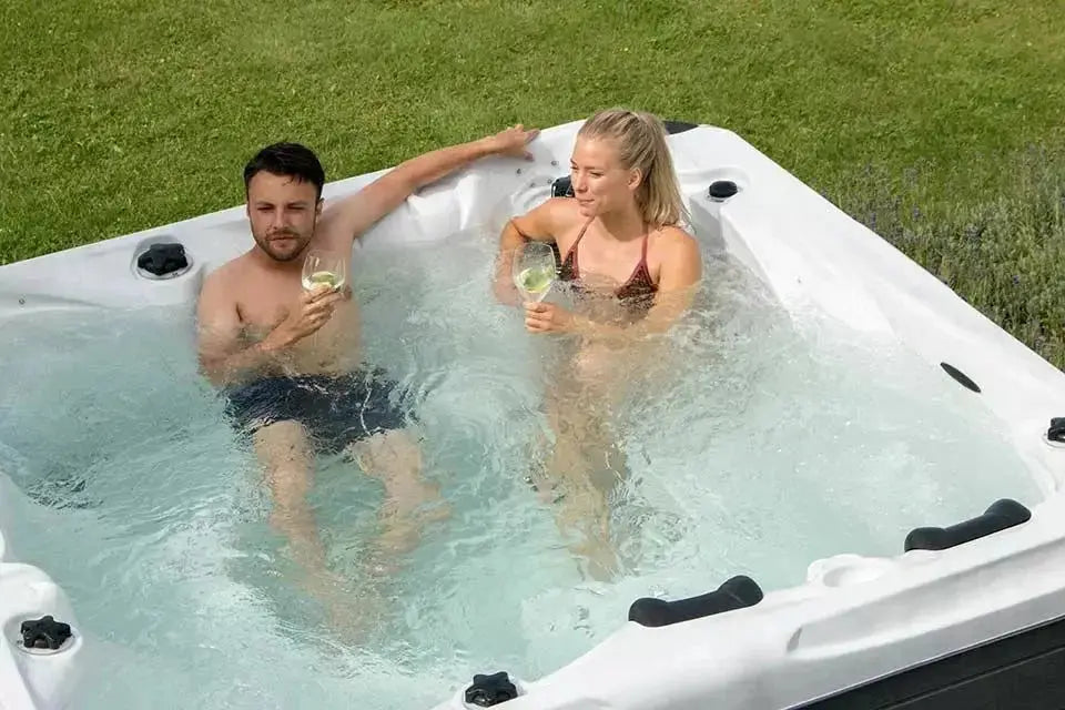 Witte jacuzzi buiten met twee personen ontspannen in een swimspa op grasveld.