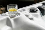 Witte jacuzzi buiten met bekerhouder en glazen waterglas gevuld met water en citroen, spa voor 5 personen.