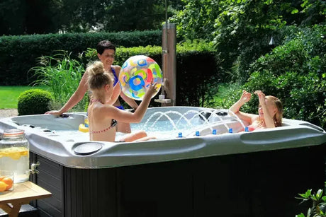 Zwarte 5-persoons jacuzzi buiten met waterjets en kinderen spelend in zwemspa.